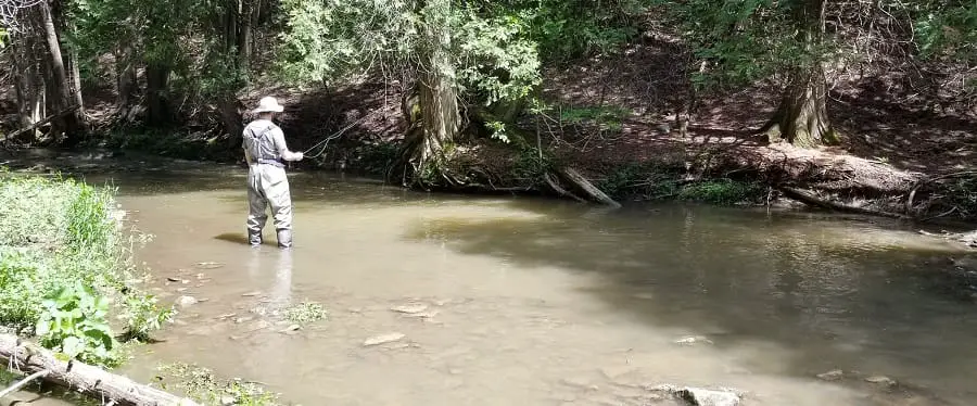 An angler fishing for trout in dirty water