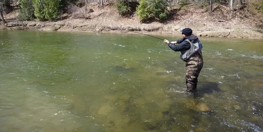 An angler fighting a steelhead while standing in the river with Neoprene waders on.