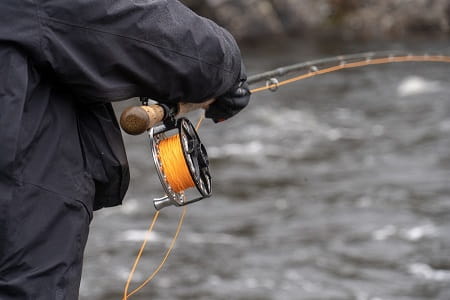 An angler holding a fly reel and rod.