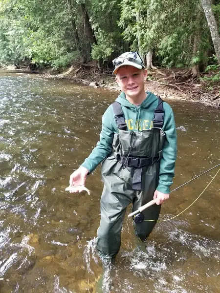 One of my young clients with a trout in hand while standing in the river in kids waders.