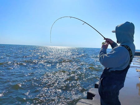 An angler fishing for salmon on a pier at the mouth a river.