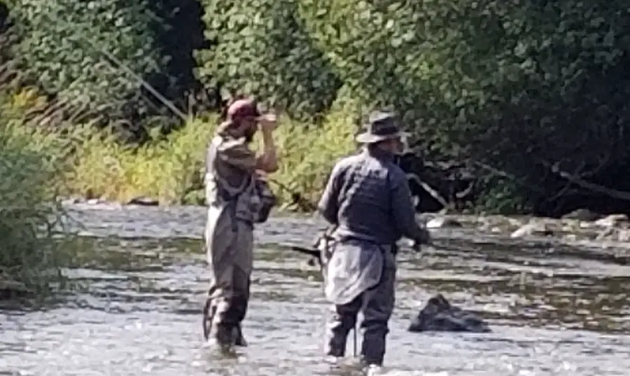 One of my guides and client standing in the river, both wearing fishing hats.