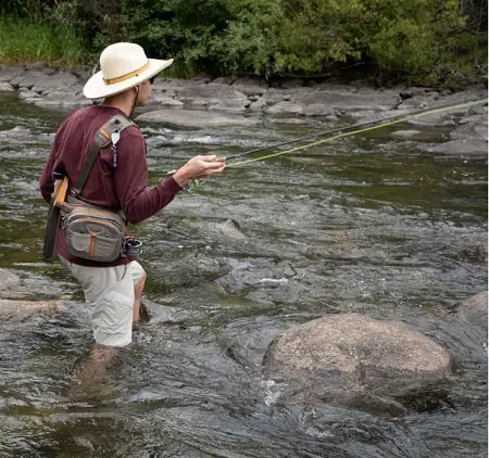 An angler in the river wearing the Fishpond Eddy River Hat.